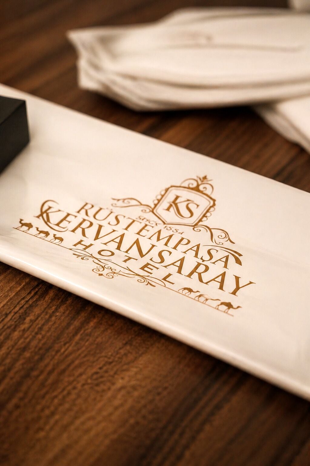 A white rectangular placemat with embossed text and decorative elements, placed on a wooden surface.