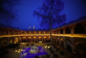 A courtyard with a fountain, arches, and a large tree.