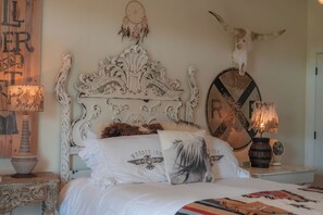 A bedroom with an ornate white headboard, a cow skull, and a dreamcatcher on the wall. - The Wanderlust Room - Wander Inn (Round Top)