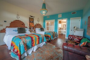 A room with two beds, a chandelier, a wooden headboard, a colorful rug, and a leather couch. - The Bandita Room - Wander Inn (Round Top)