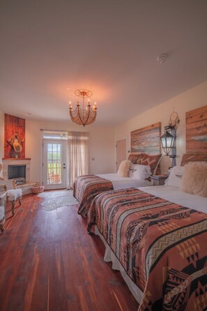 Two double beds with patterned bedspreads, a chandelier, and a fireplace are featured in this traditional bedroom.