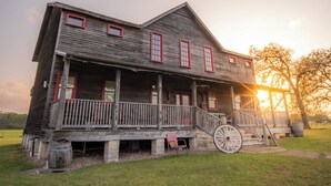 A rustic wooden house with a porch and a large wheel, set in a grassy area. - The Stardust Room - Wander Inn (Round Top)