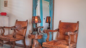 A room with two wooden chairs with leather seats and backs, a blue-framed mirror, and two table lamps with stained glass shades.