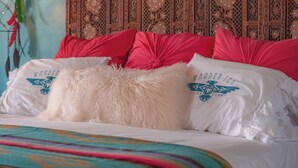 A bed with a colorful blanket, red pillows, and a wooden headboard with intricate carvings.