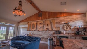 A cozy living room with a large wooden wall, a blue sofa, a wooden dining table, and a chandelier. - The Rambler Room - Wander Inn (Round Top)