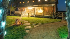 A rustic wooden house with a porch, illuminated by string lights and a crown-shaped light fixture. - The Rambler Room - Wander Inn (Round Top)