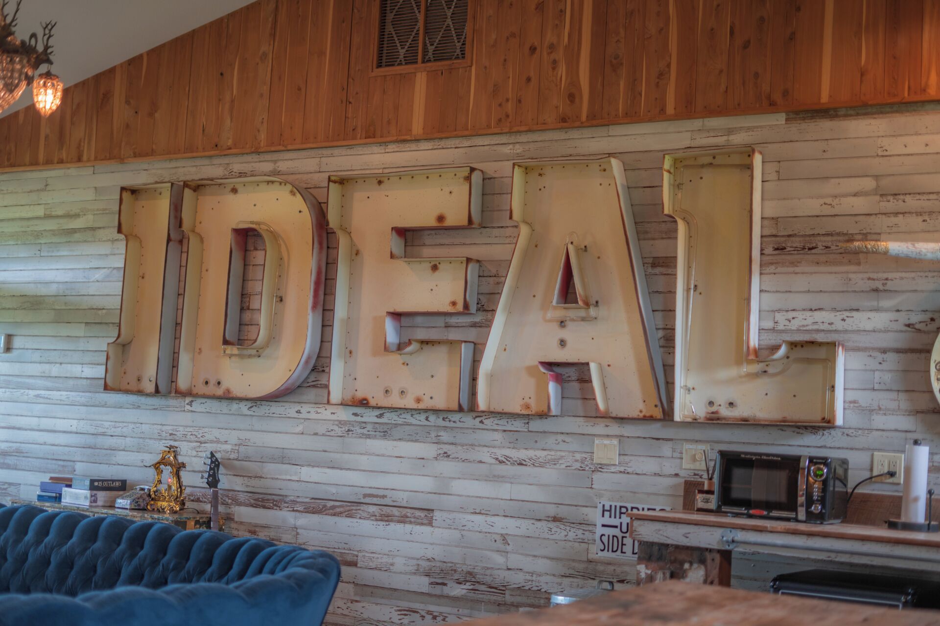 A rustic interior with wooden walls, a blue sofa, and a sign reading "IDEAL".