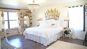 A bedroom with a large bed, a chandelier, a mirror, and a window with curtains. - Gypsy Farmhouse - Wander Inn (Round Top)
