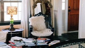 A cozy living room with a patterned ceiling, a rustic chair, a mirror with an ornate frame, and a door leading to another room. - Gypsy Farmhouse - Wander Inn (Round Top)
