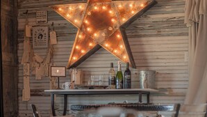 A rustic interior with a wooden wall, a star-shaped light fixture, a bar area with bottles and glasses, and a table with chairs. - Thelma's Garage - Wander Inn (Round Top)