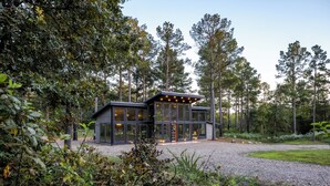 A modern house with large glass windows, surrounded by a forest. - 2Bdr with elevated design and bunkhouse! (Broken Bow)