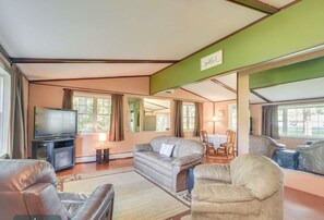 A living room with a television, leather sofas, a coffee table, and a dining table with chairs. - Furnished Lakeside Home (Webster)