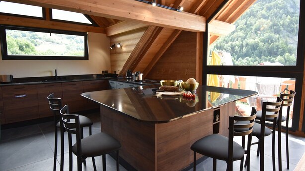 A modern kitchen with a central island, bar stools, and a large window offering a view of the forest. - Chalet Sert et Sagne 1 (Vaujany)