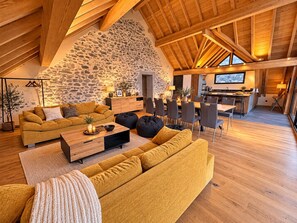 Un loft spacieux avec de hauts plafonds, un mur en pierre, des poutres en bois, un coin repas et une cuisine.