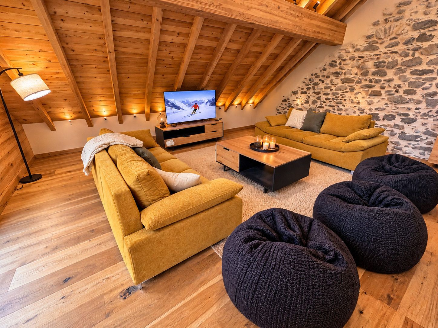 A cozy living room with a wooden ceiling, a flat-screen TV, a sofa, a coffee table, and bean bags.