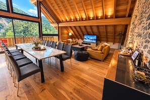 Un grand espace de vie doté d’un plafond en bois, d’un téléviseur, d’un canapé et d’une table à manger avec des chaises.