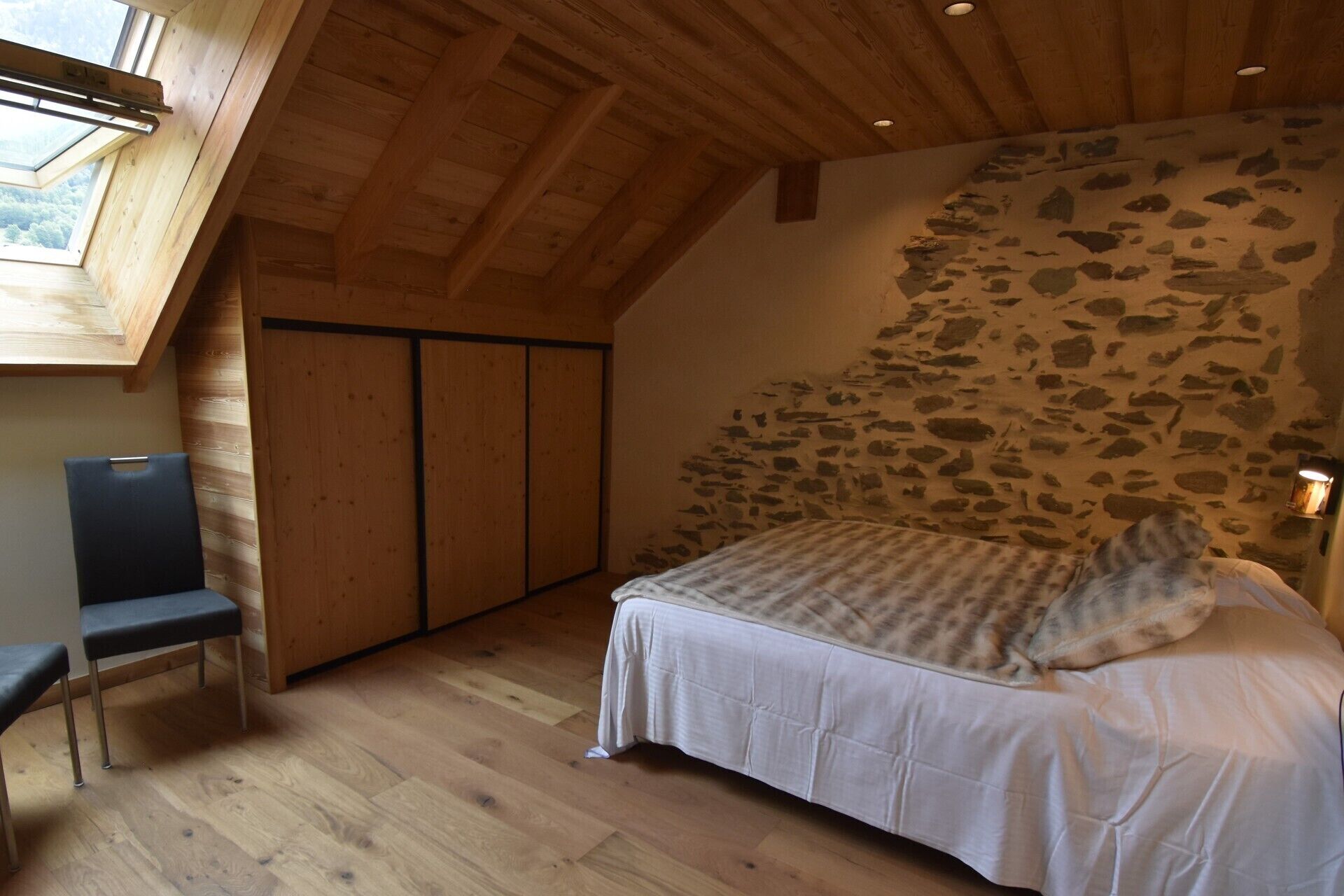 Un dormitorio con pared de piedra, techo de madera y cama con colcha estampada.