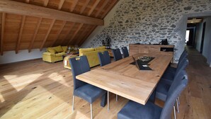 A spacious loft with a high wooden ceiling, stone walls, a wooden dining table with chairs, and a yellow sofa. - Chalet Sert et Sagne 1 (Vaujany)