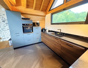 Eine moderne Küche mit Holzschränken, einem eingebauten Backofen und einem großen Fenster mit Blick auf Grünflächen.