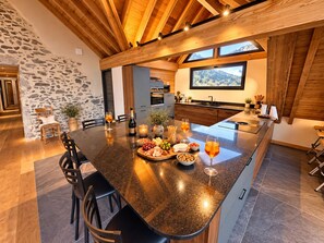 Une cuisine moderne dotée d’un grand îlot central, d’un mur en pierre et offrant une vue sur les montagnes.