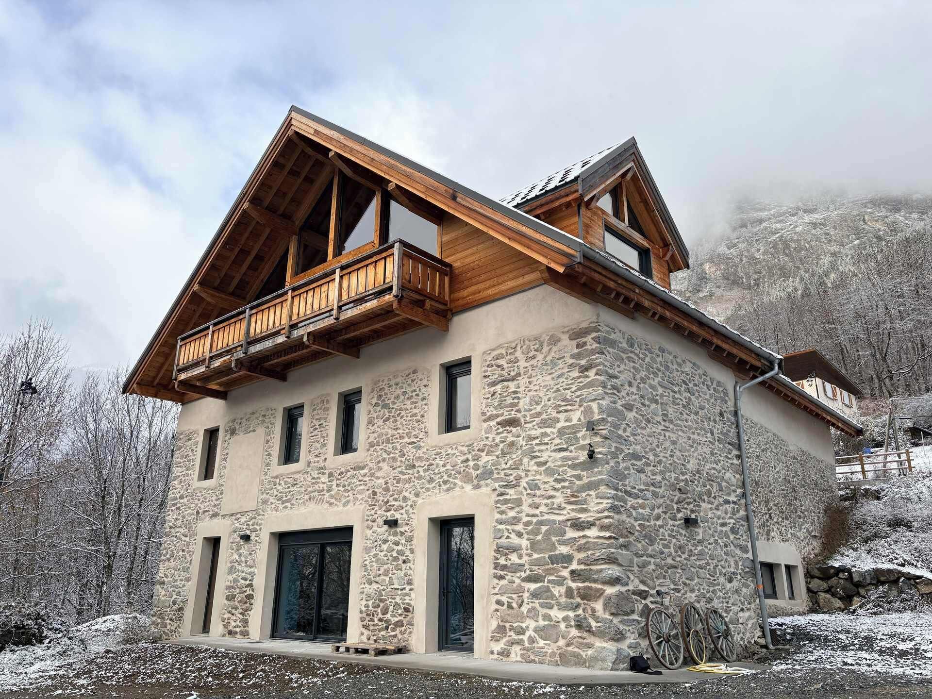 Un edificio de piedra con un balcón de madera, varias ventanas y un paisaje montañoso al fondo.