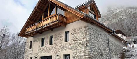 Un edificio de piedra con un balcón de madera, varias ventanas y un paisaje montañoso al fondo.