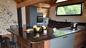A modern kitchen with a central island, wooden cabinets, and a large window. - Chalet Sert et Sagne 1 (Vaujany)