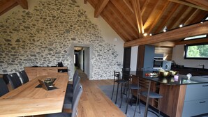 A modern kitchen with a stone wall, wooden dining table, and bar area. - Chalet Sert et Sagne 1 (Vaujany)