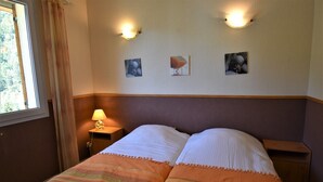 A double bed with striped bedding, a nightstand with a lamp, and wall-mounted artwork. - Chalet Roches Grandes 47 (Vaujany)