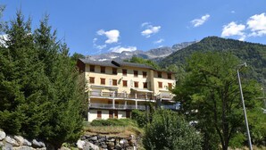 A multi-story building with balconies, surrounded by trees and mountains in the background. - Chalet Roches Grandes 49 (Vaujany)