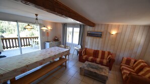 A cozy living area with a wooden bench, a sofa, and a dining table with a floral tablecloth. - Chalet Roches Grandes 49 (Vaujany)