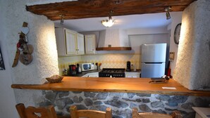 A rustic kitchen with a stone wall, wooden bar counter, and three wooden chairs. - Chalet Roches Grandes 49 (Vaujany)