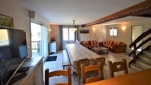 A spacious living area with a long dining table, a sofa, and a TV in the corner. - Chalet Roches Grandes 49 (Vaujany)