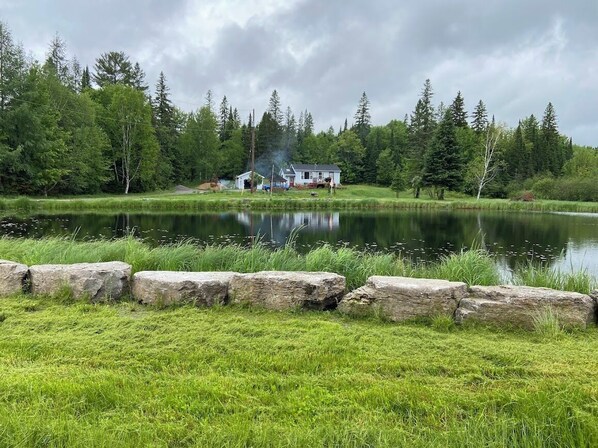 Una cabaña junto al lago con un muelle, rodeada de un bosque denso y un lago tranquilo.