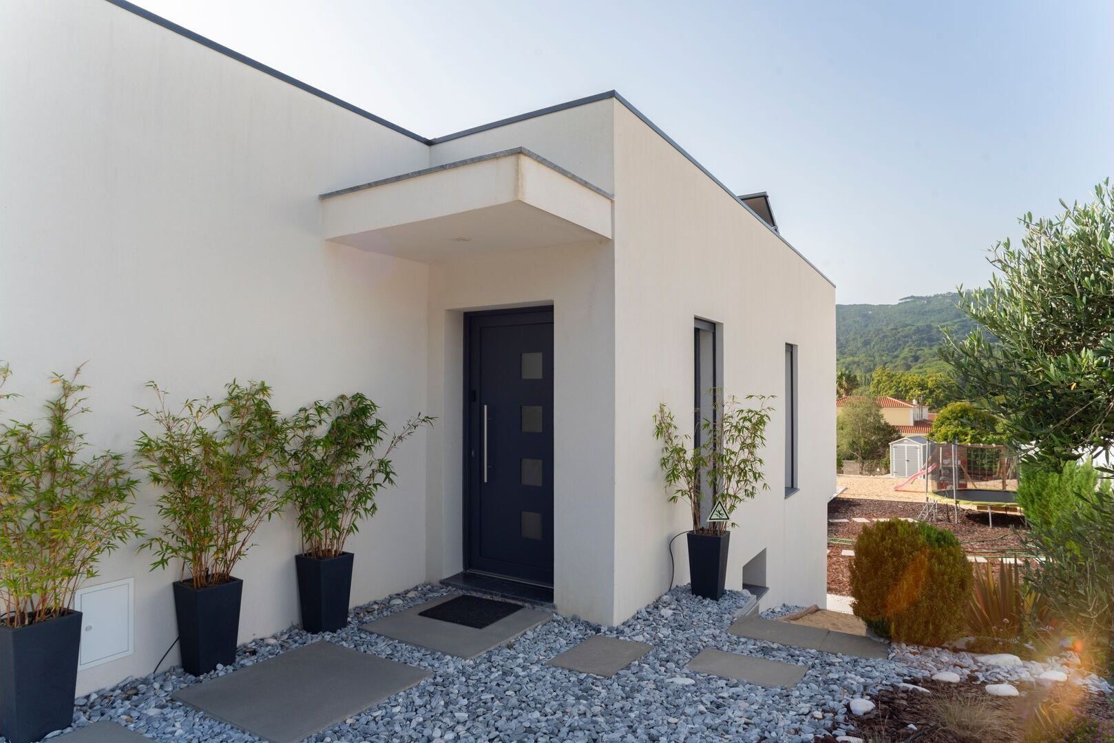 A modern house with a white exterior, a dark door, and potted plants.
