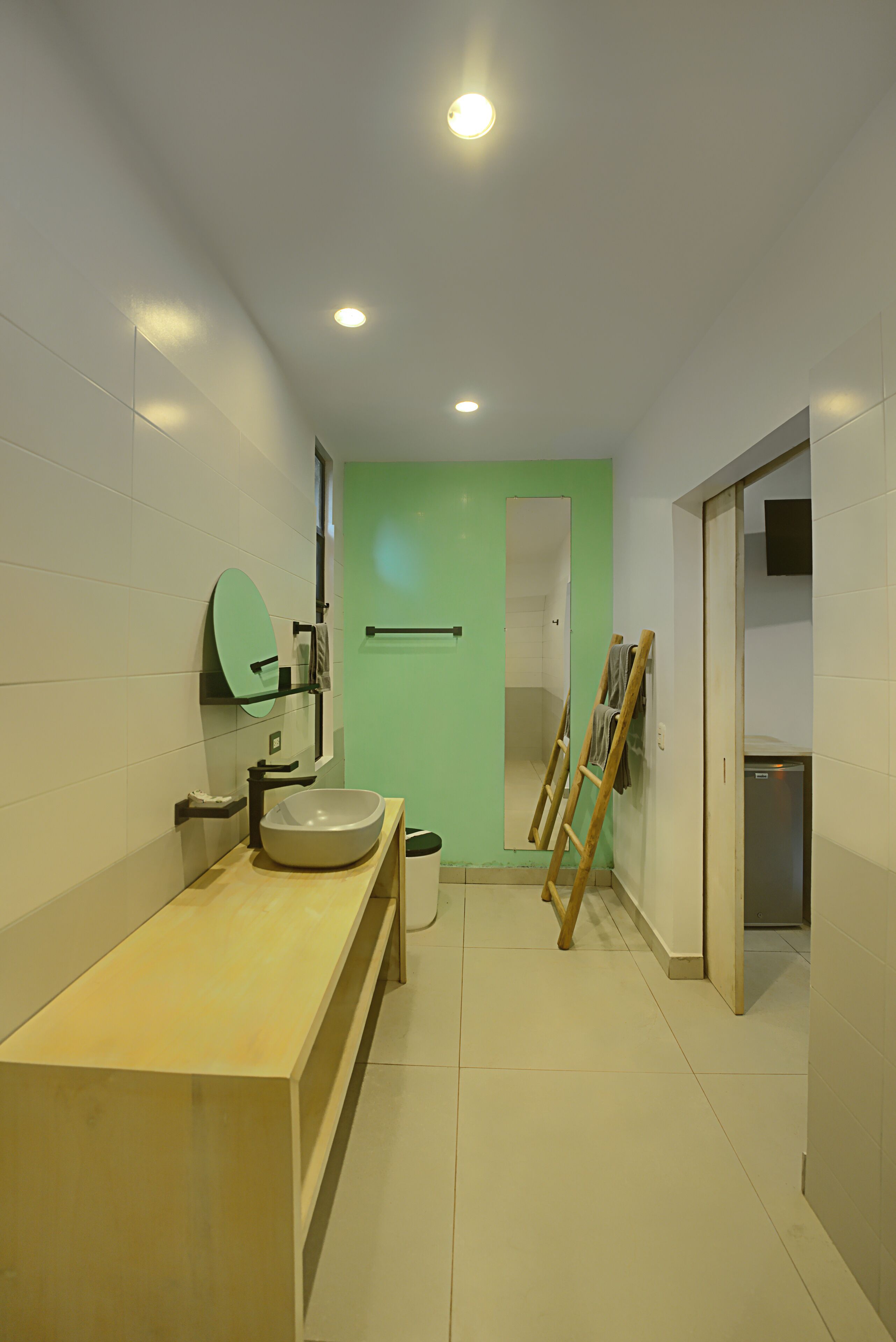 A modern bathroom with a large sink, mirror, and a green door leading to another room.