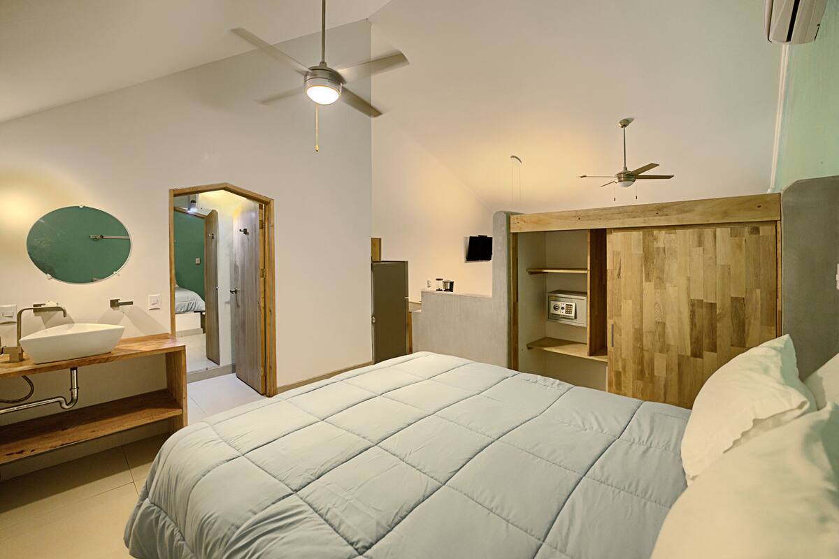 Un dormitorio moderno con una cama, cabecera de madera, mesita de noche, espejo y ventilador de techo.