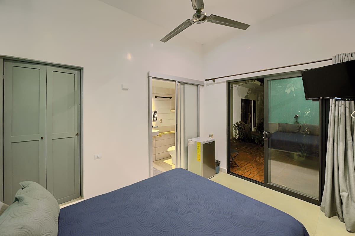 Un dormitorio con cama, ventilador de techo, armario y puerta corrediza de vidrio que da a un balcón.
