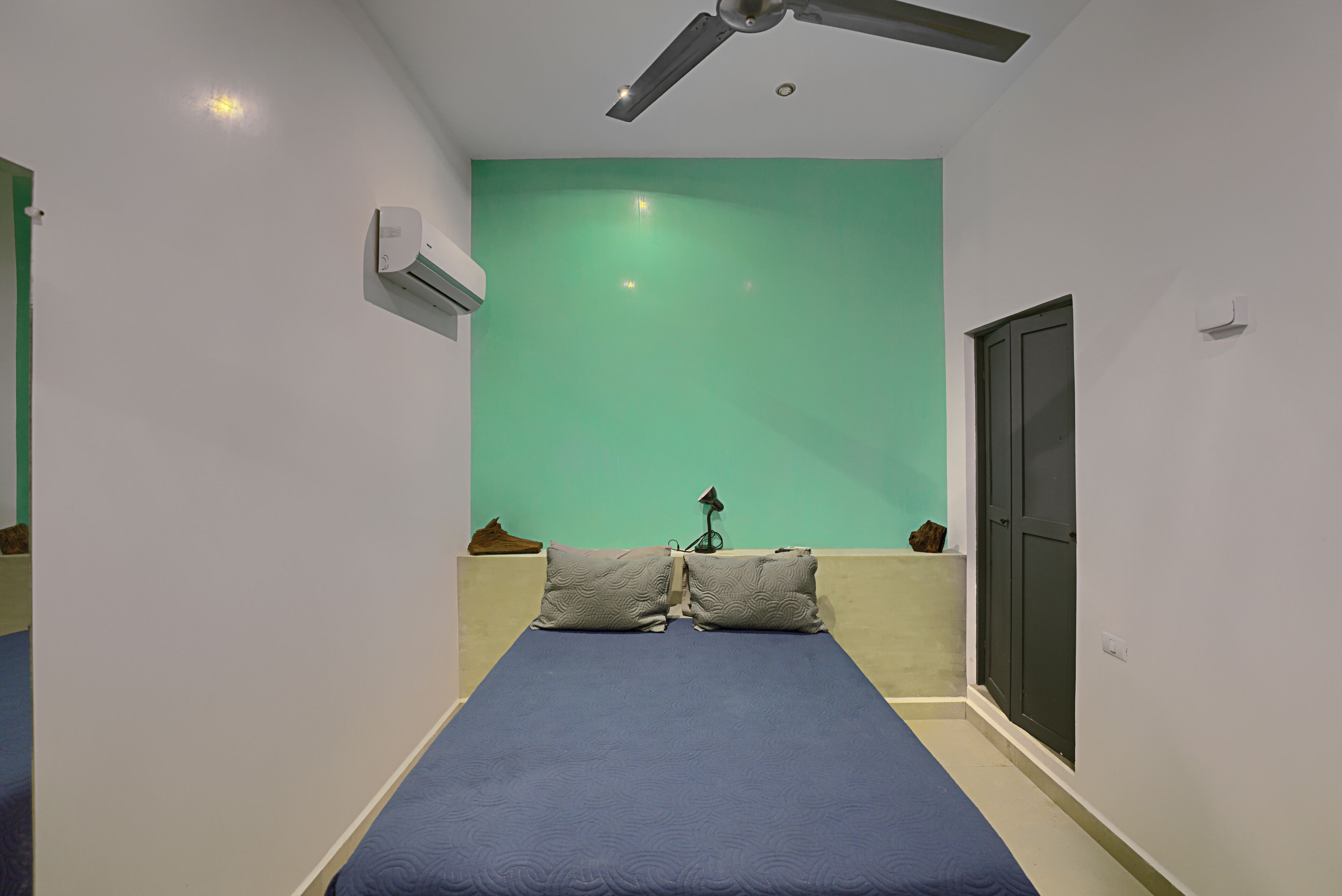 Una habitación con una cama, ventilador de techo, aire acondicionado, pared verde y una puerta.