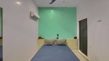 Una habitación con una cama, ventilador de techo, aire acondicionado, pared verde y una puerta.
