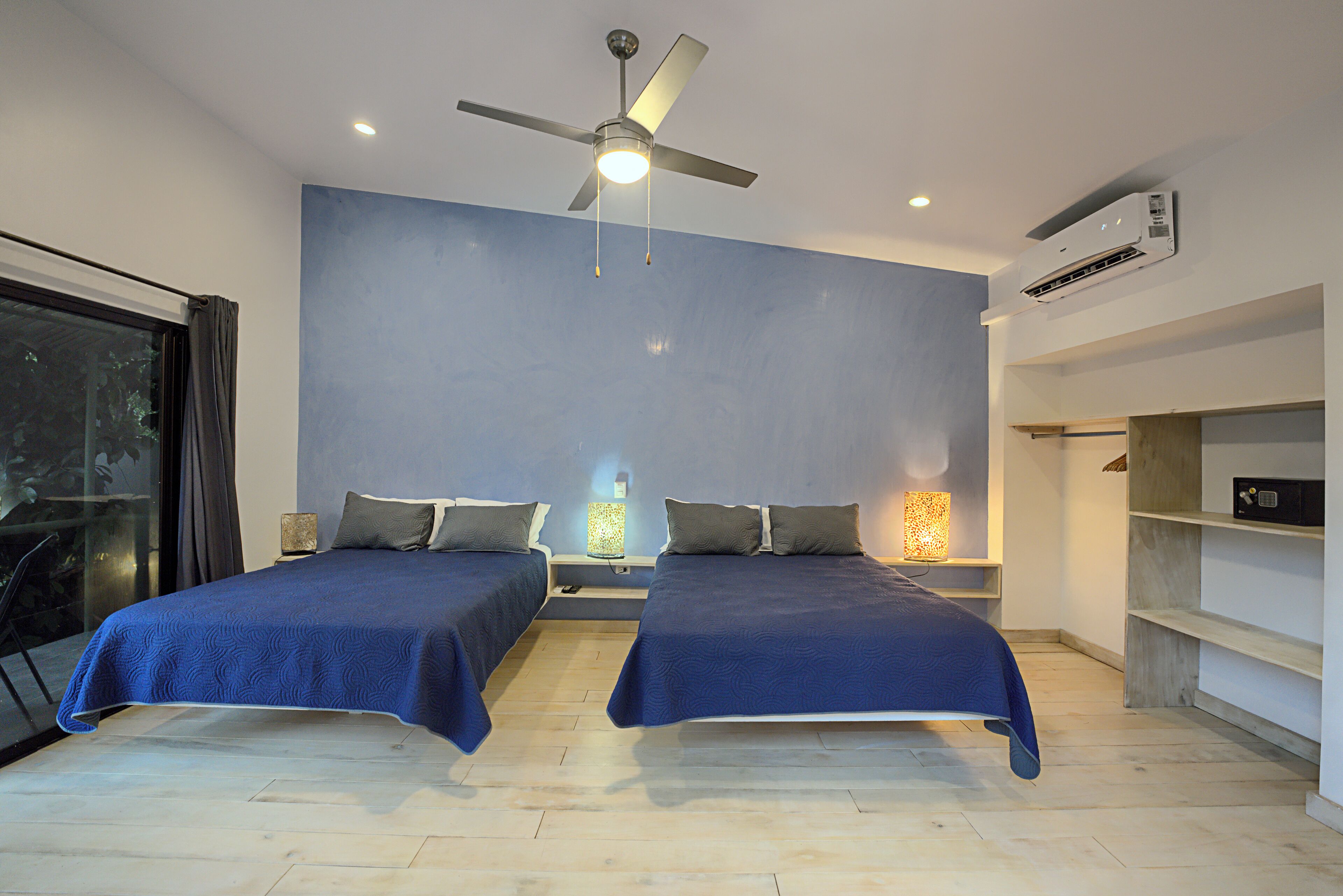 A modern bedroom with two beds, a ceiling fan, and built-in shelving.