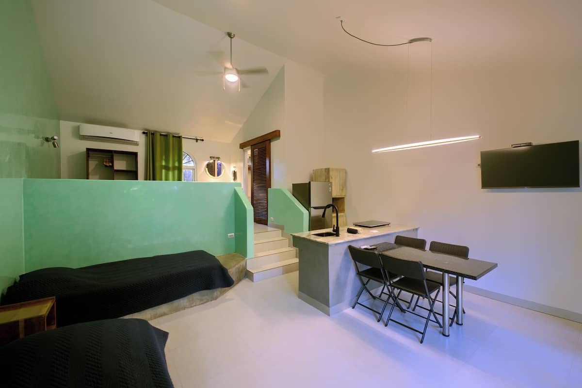 Una habitación compacta con kitchenette, un comedor con mesa y sillas, y una cama.