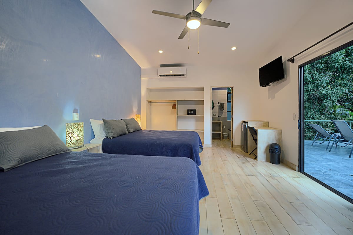 Habitación de hotel moderna con dos camas, ventilador de techo, televisión y vistas al exterior.