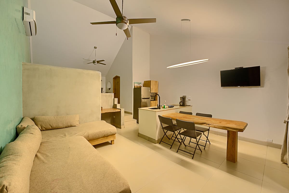 Un espacio habitable moderno y funcional con sofá, mesa de comedor y televisor montado en la pared.