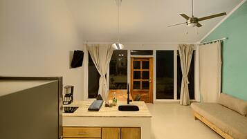 A modern living room with a sofa, a coffee maker, and a small kitchen area.