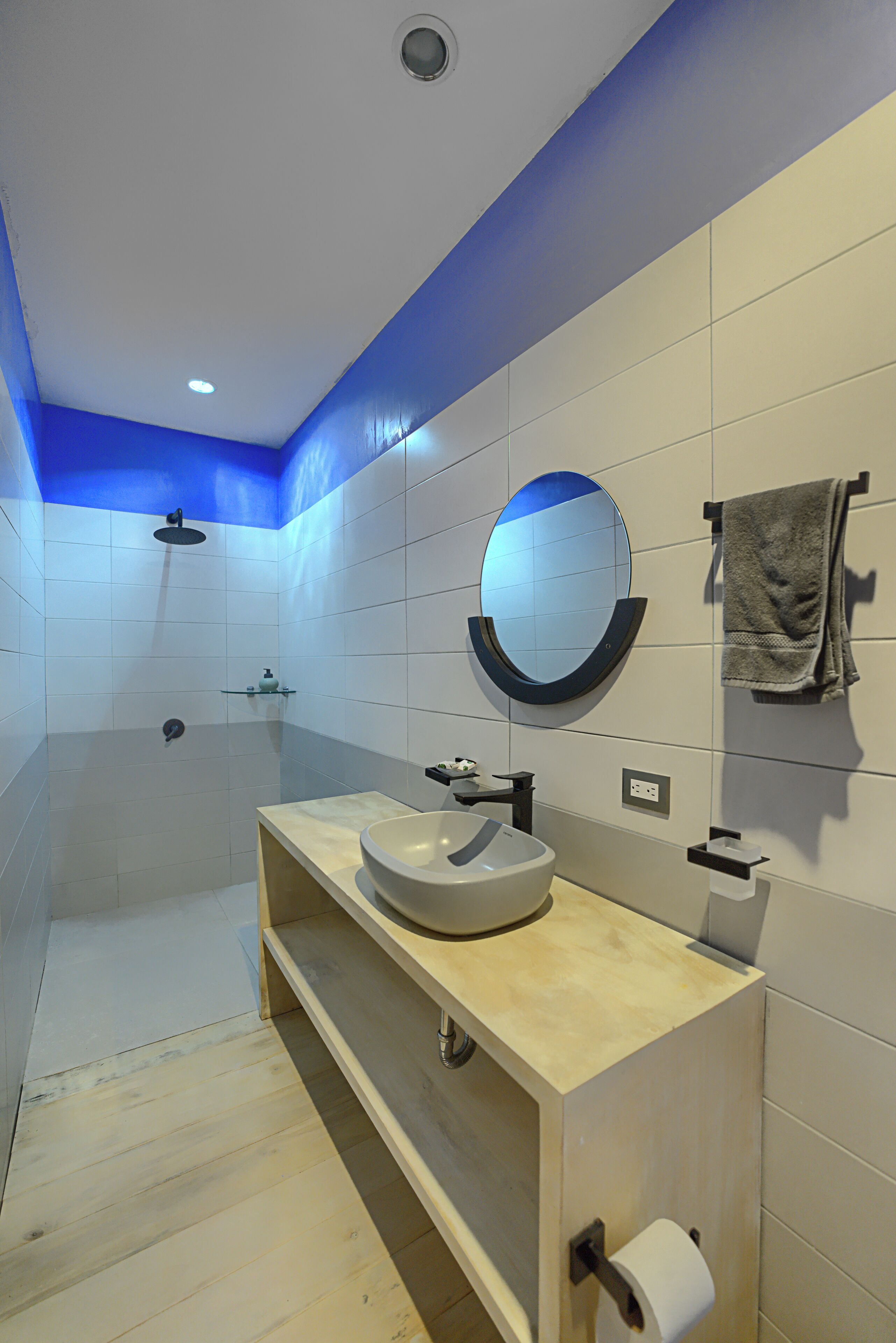 A modern bathroom with a wooden vanity, a round mirror, a towel rack, and a shower area.