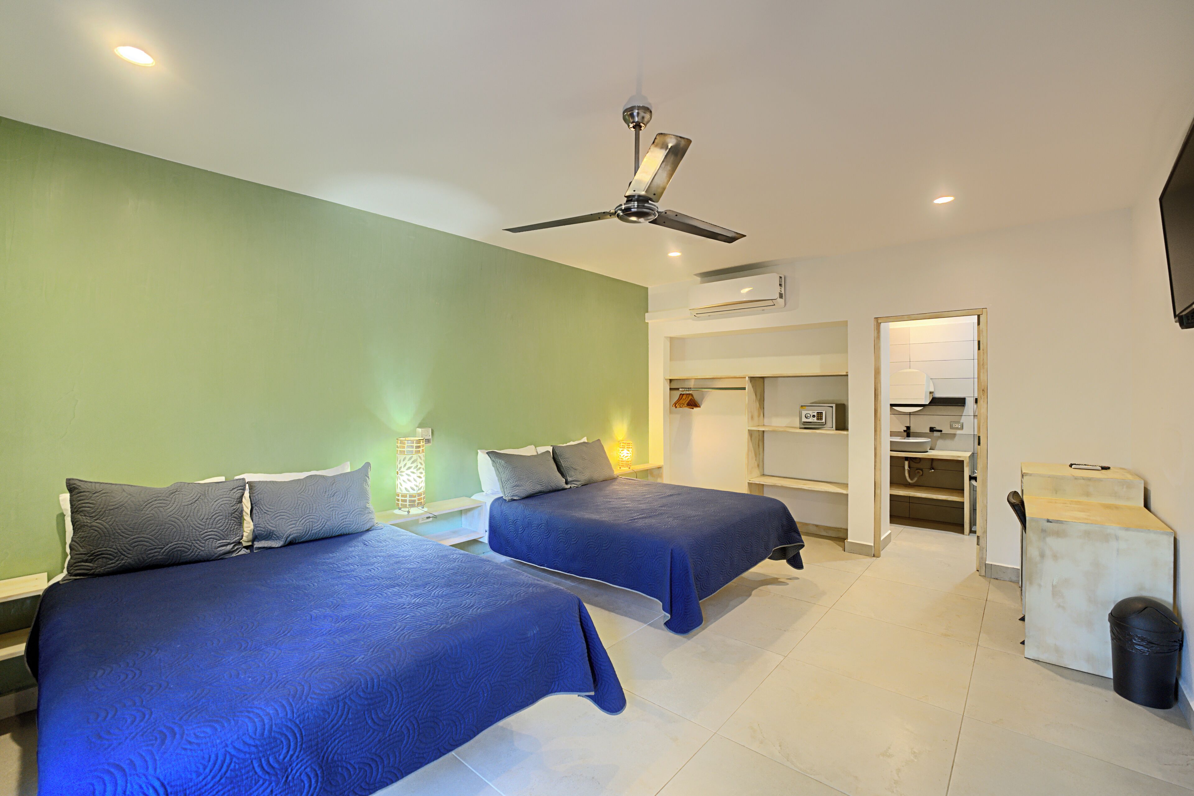 A hotel room with two beds, a ceiling fan, a kitchenette, and a trash bin.