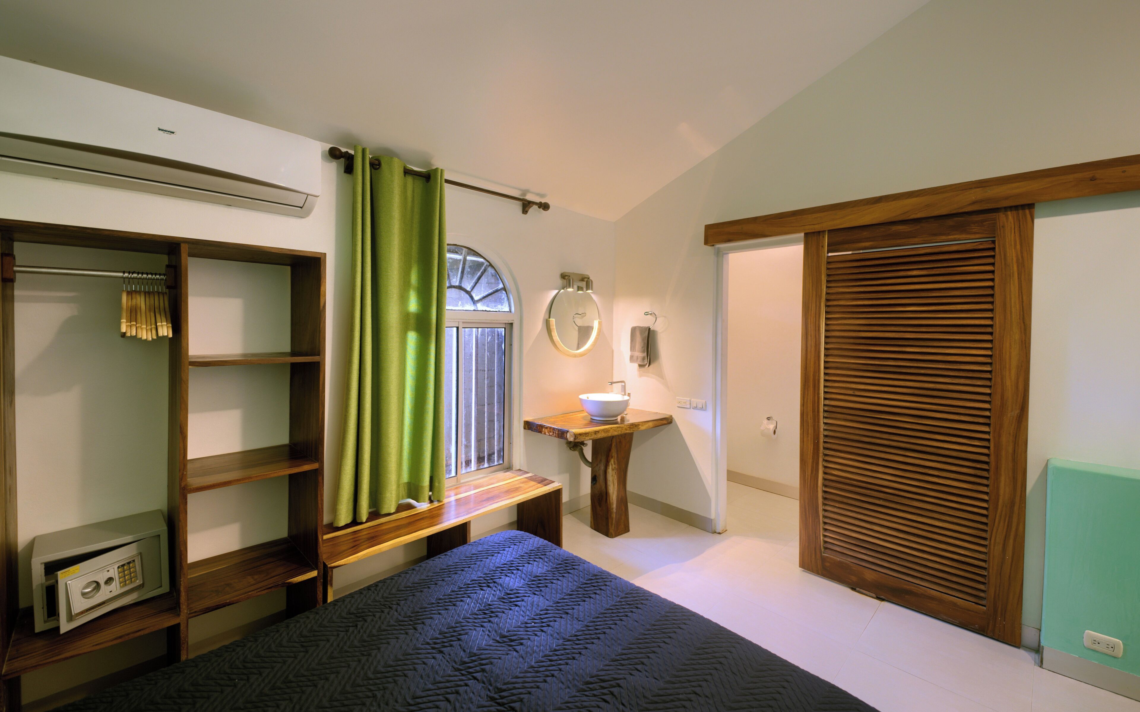 Une chambre à coucher avec un lit, une armoire en bois, une coiffeuse avec un miroir et un rideau vert.