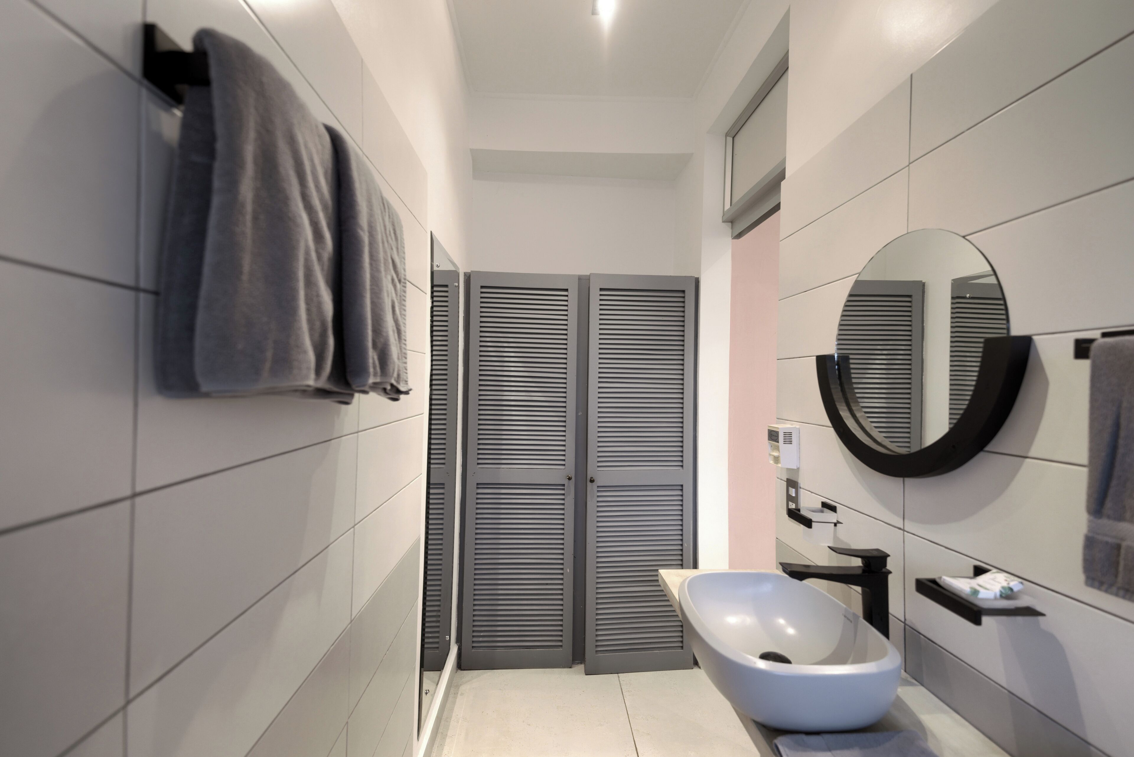 Un baño moderno con paredes de azulejos grises, un lavabo blanco, un espejo grande y una bañera empotrada.