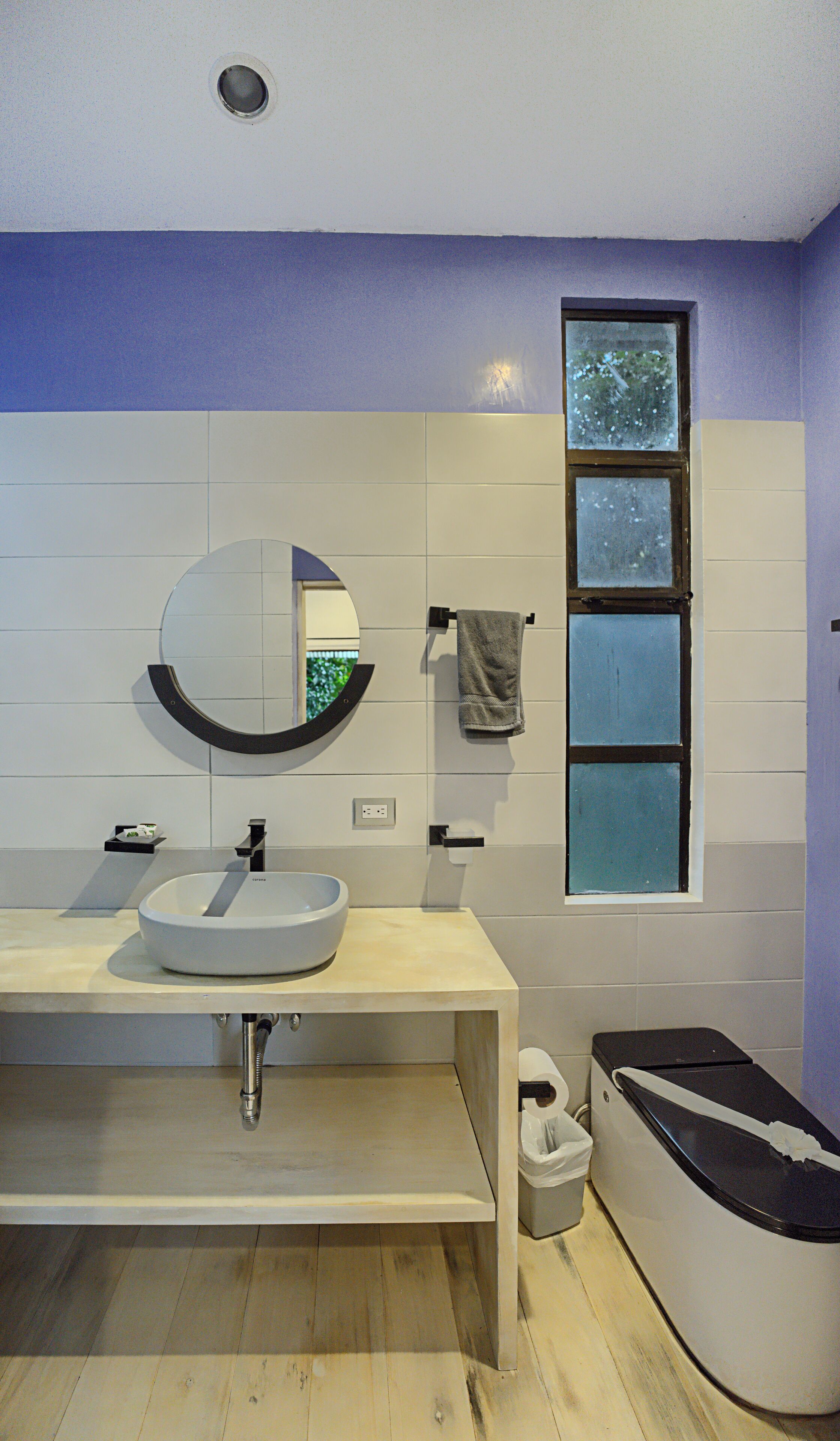 A modern bathroom with a round mirror, a sink, and a window.